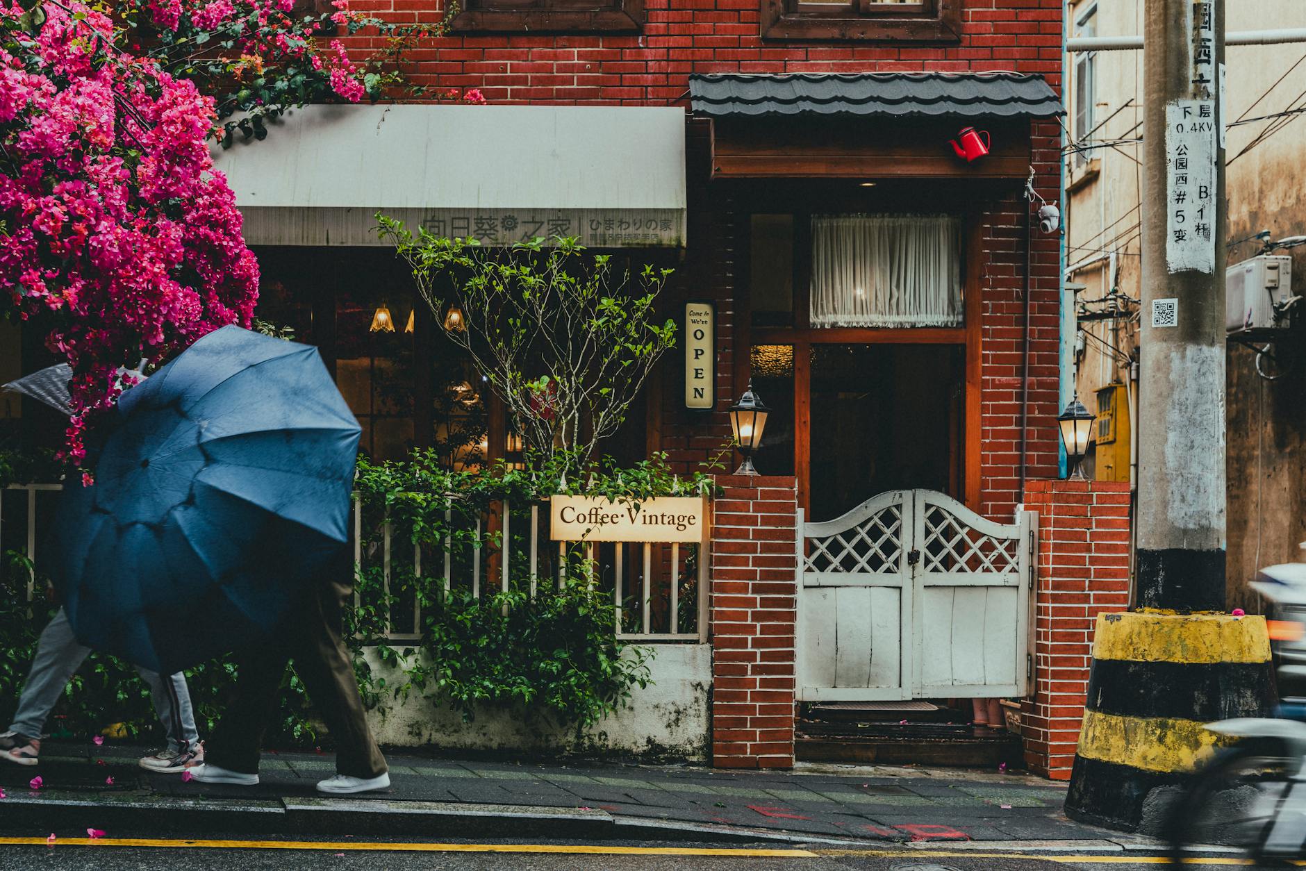 pedestrians with umbrella walking by brick house in city